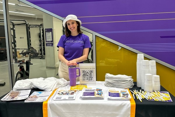 person in LSU shirt stands behind a table with an LSU banner on it