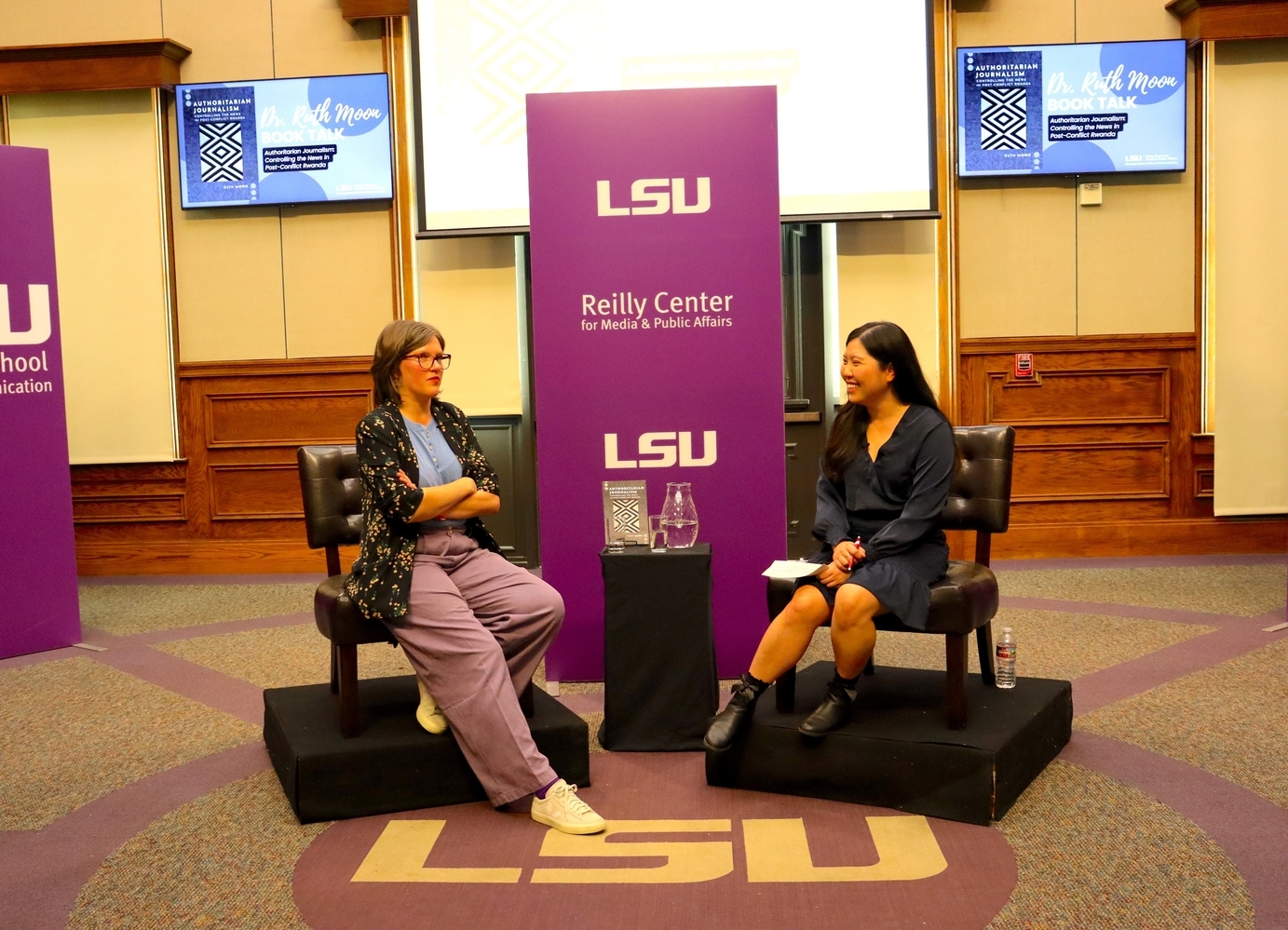 An image of the front of the Holliday Forum with event moderator to the right and guest speaker, Ruth Moon, on the left sitting in front of a Reilly Center sign.