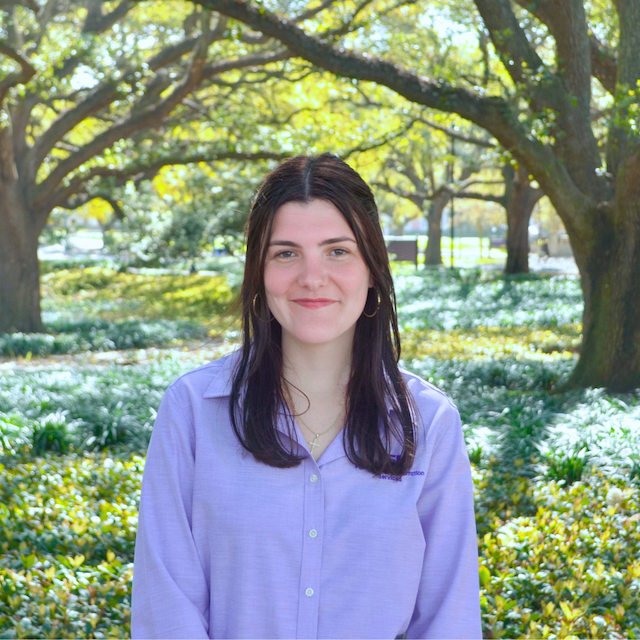 woman smiling in purple polo in front of trees